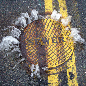 An SSO spills out from beneath a manhole cover.  Photo: Mystic River Watershed Association, “Sewer overflowing.”