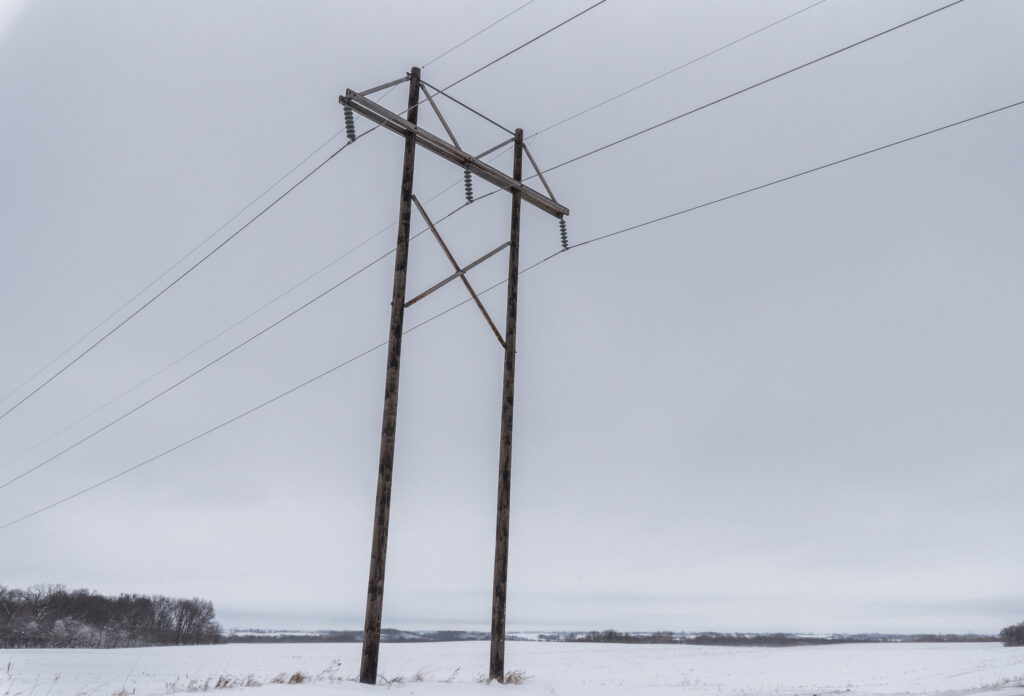 Power lines against a snowy field and gray sky.