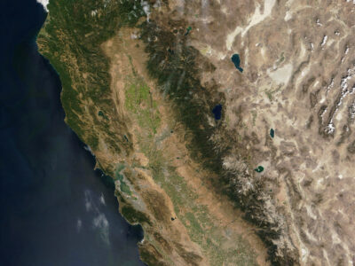 Satellite image of California, centered on the Bay-Delta watershed. The Central Valley shows up prominently, with green agricultural fields rimmed by drier brown land, surrounded by mountains.