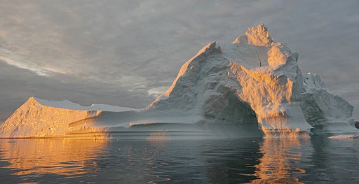 Image shows a sunlit melting iceberg against a cloudy sky