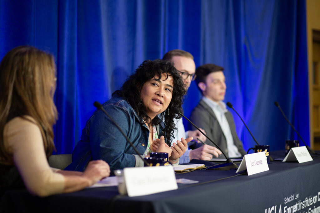 Four panelists sit on stage in front of a bright blue curtain.