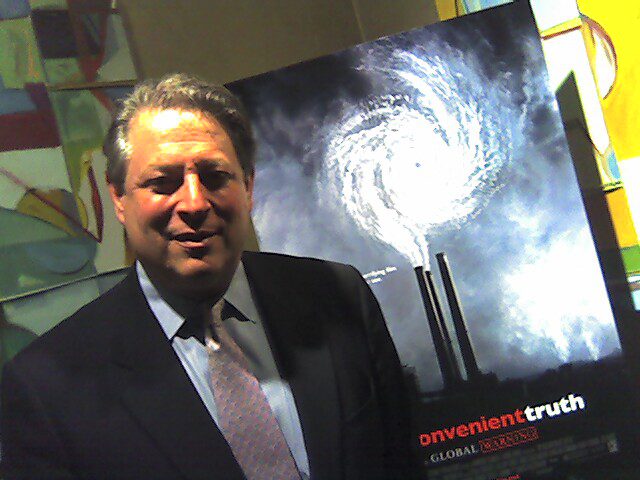 A man stands in front of a movie poster showing smoke coming out of factory plumes and the smoke converting into a hurricane.