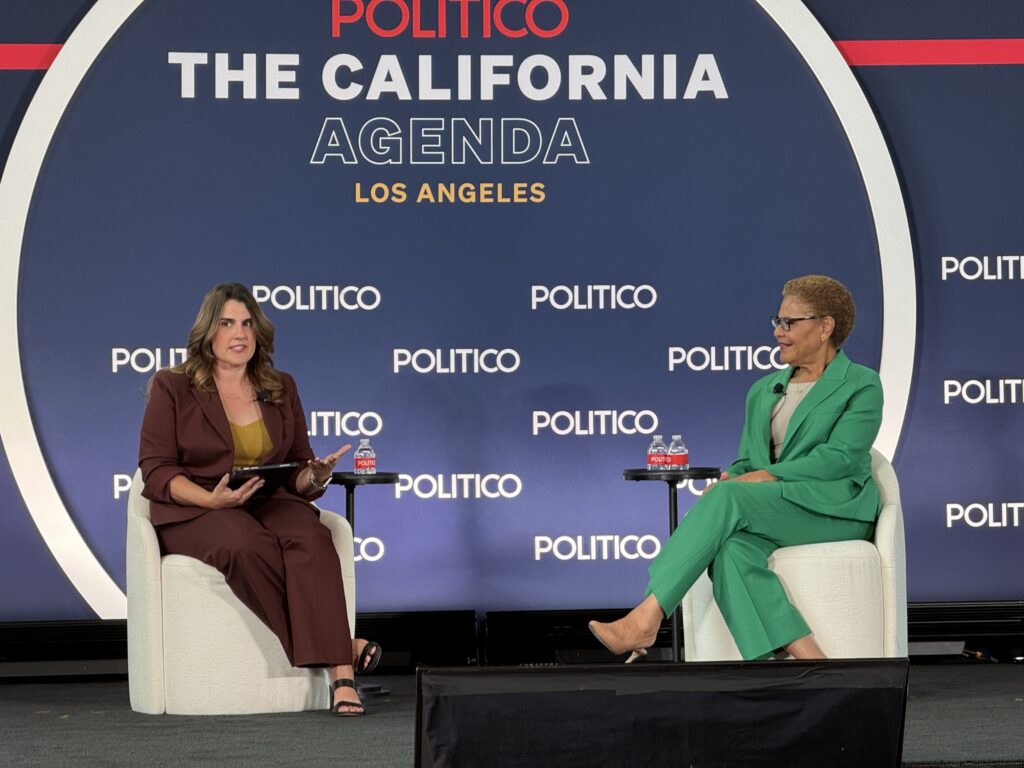 Two women sit on stage in armchairs during a POLITICO “The California Agenda” event in Los Angeles. One woman holds a tablet and speaks while the other listens. A backdrop displays the event name and sponsorship.