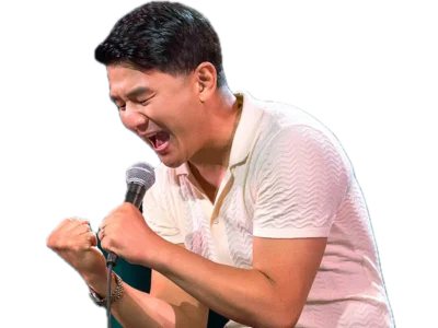 A man in a white shirt passionately sings or shouts into a microphone, eyes closed and fists clenched, expressing intense emotion.