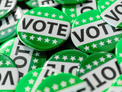 A pile of green buttons featuring the word VOTE in bold black letters and white stars on a green stripe.