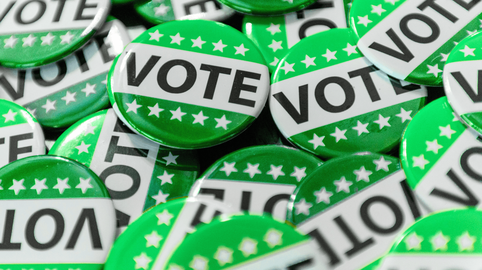 A pile of green buttons featuring the word VOTE in bold black letters and white stars on a green stripe.