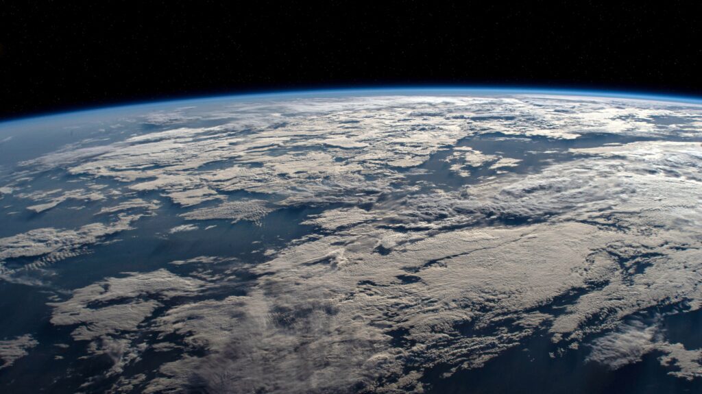 Earth seen from space, showing the planets curved horizon and cloud-covered surface against the black sky.