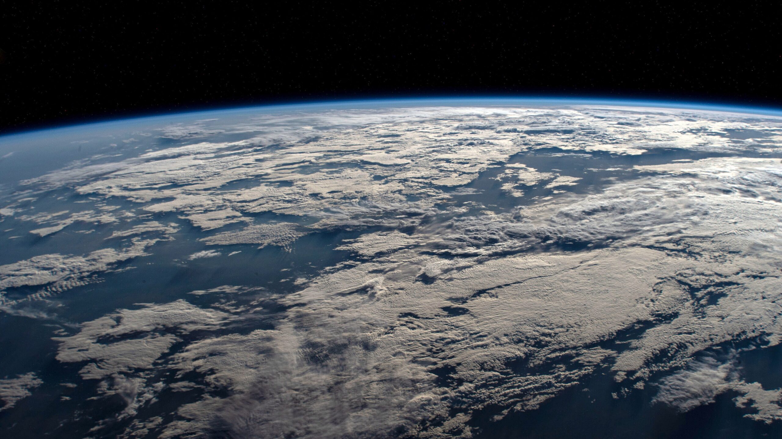 Earth seen from space, showing the planets curved horizon and cloud-covered surface against the black sky.