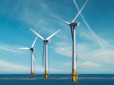 Three offshore wind turbines stand in the ocean under a blue sky.