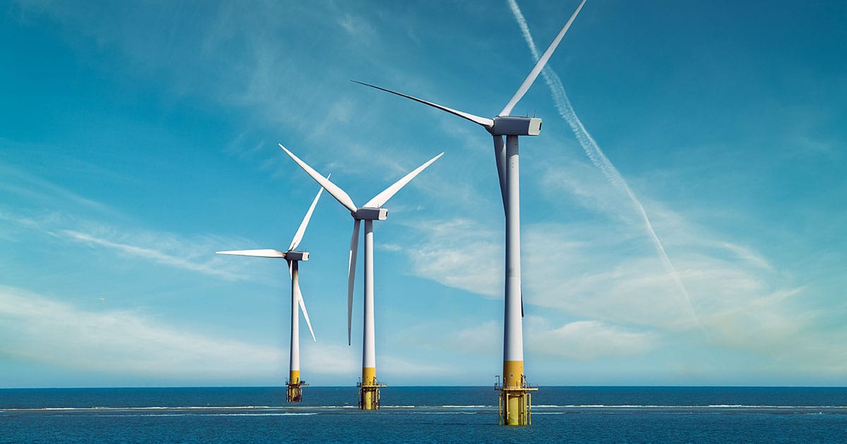 Three offshore wind turbines stand in the ocean under a blue sky.