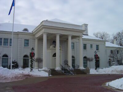 A large white building with tall pillars at the entrance, surrounded by snow and decorated with holiday wreaths.
