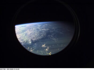 The Earths horizon, clouds, and atmosphere viewed through a circular International Space Station window.